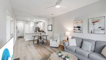 A modern living room with a grey sofa, a round coffee table, and a dining area with a table and chairs.