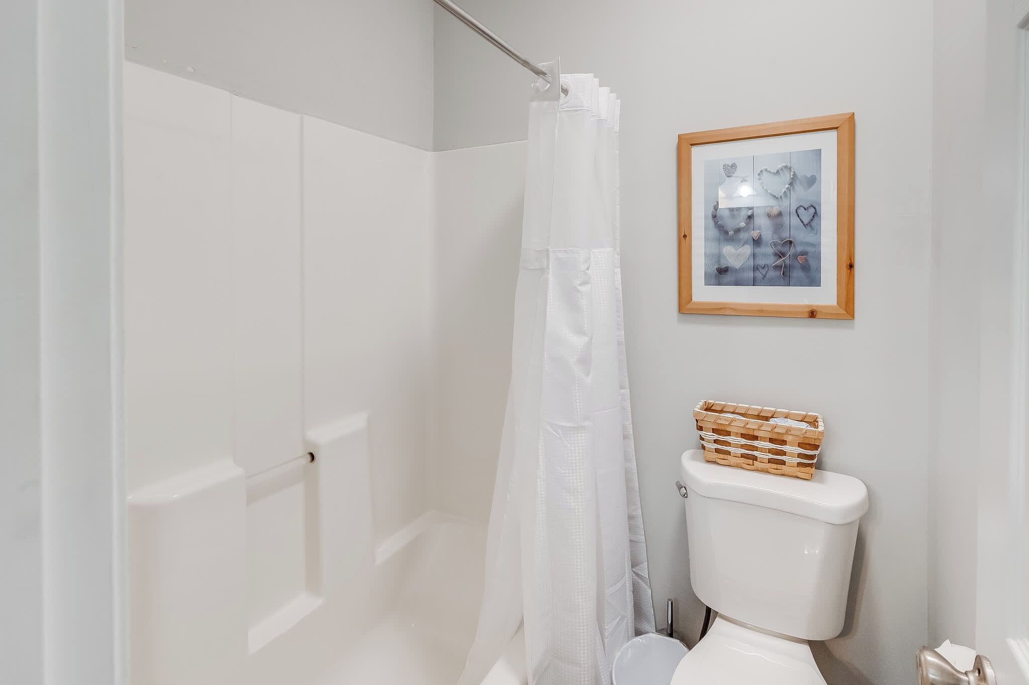 A bathroom with a white toilet, a shower curtain, and a framed picture on the wall.