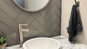 Een badkamer met een rond wastafel, een spiegel, een handdoekhouder en een potplant.