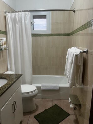 A bathroom with a toilet, bathtub, shower curtain, towel rack, and a small window. - Charming 1-bedroom apartment, near the Airport, great for travel connections (Nassau)