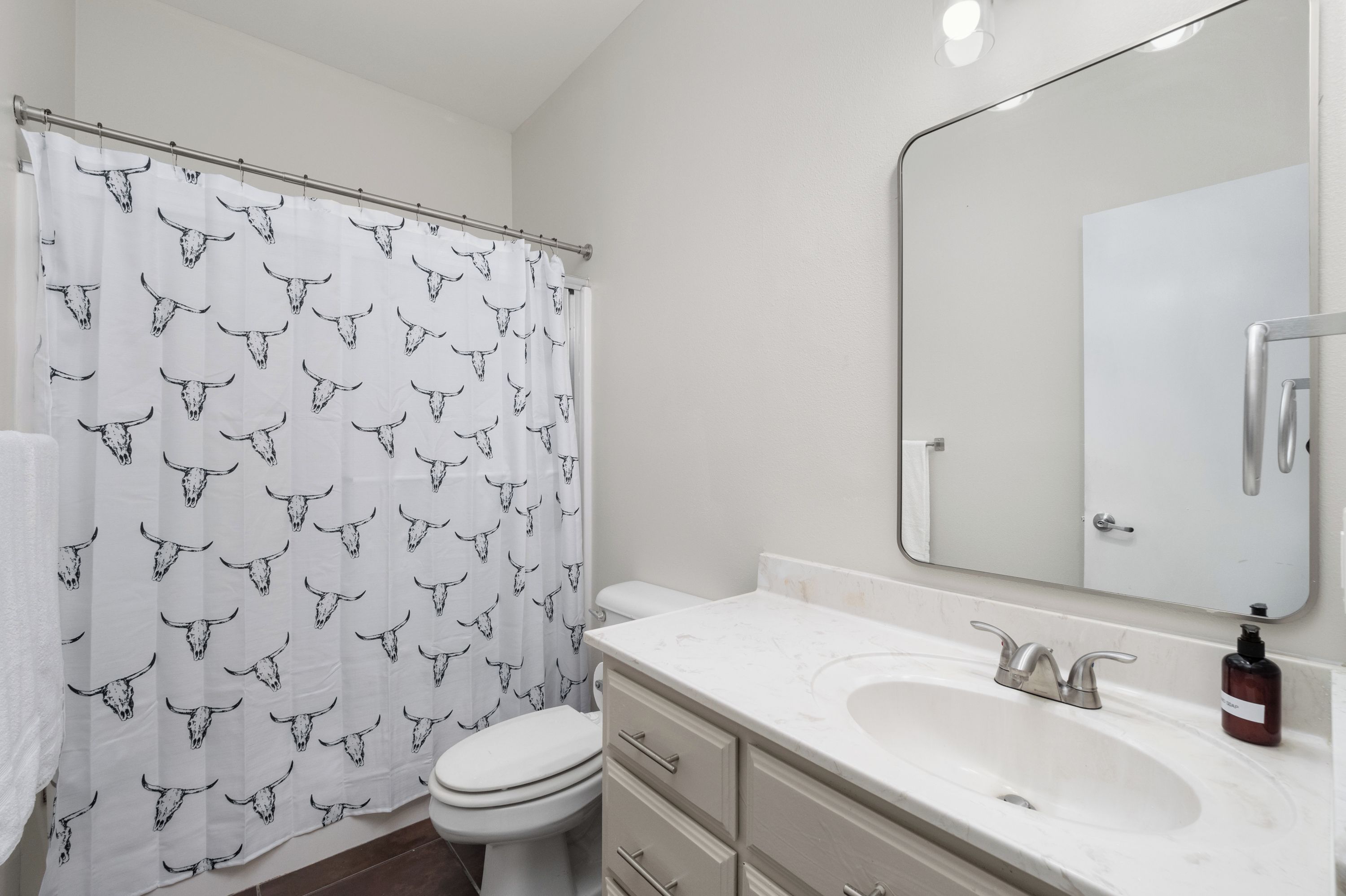 A bathroom with a white toilet, a sink with a mirror, and a shower curtain with a bull pattern.