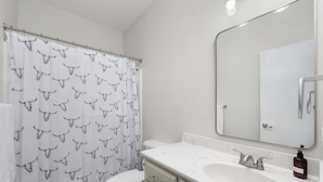 A bathroom with a white toilet, a sink with a mirror, and a shower curtain with a bull pattern. - The A Lux Backyard House | 3BR w Private Backyard (Brownsville)