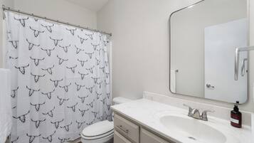 A bathroom with a white toilet, a sink with a mirror, and a shower curtain with a bull pattern.
