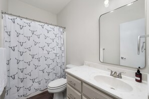 A bathroom with a white toilet, a sink with a mirror, and a shower curtain with a bull pattern. - The A Lux Backyard House | 3BR w Private Backyard (Brownsville)