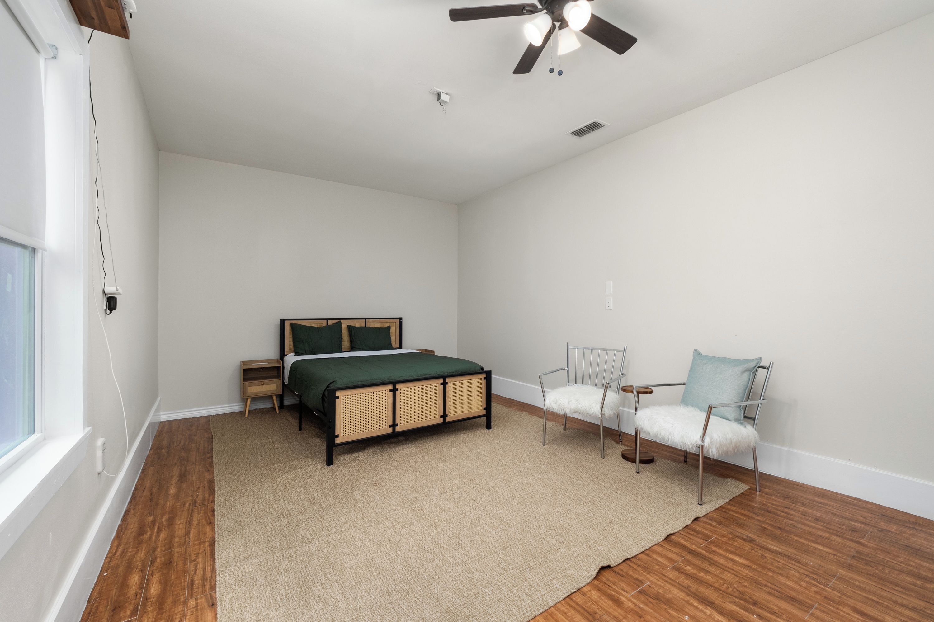 A bedroom with a bed, two chairs, a ceiling fan, and a window.