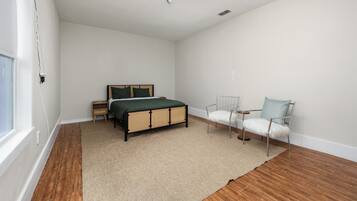 A bedroom with a bed, two chairs, a ceiling fan, and a window.