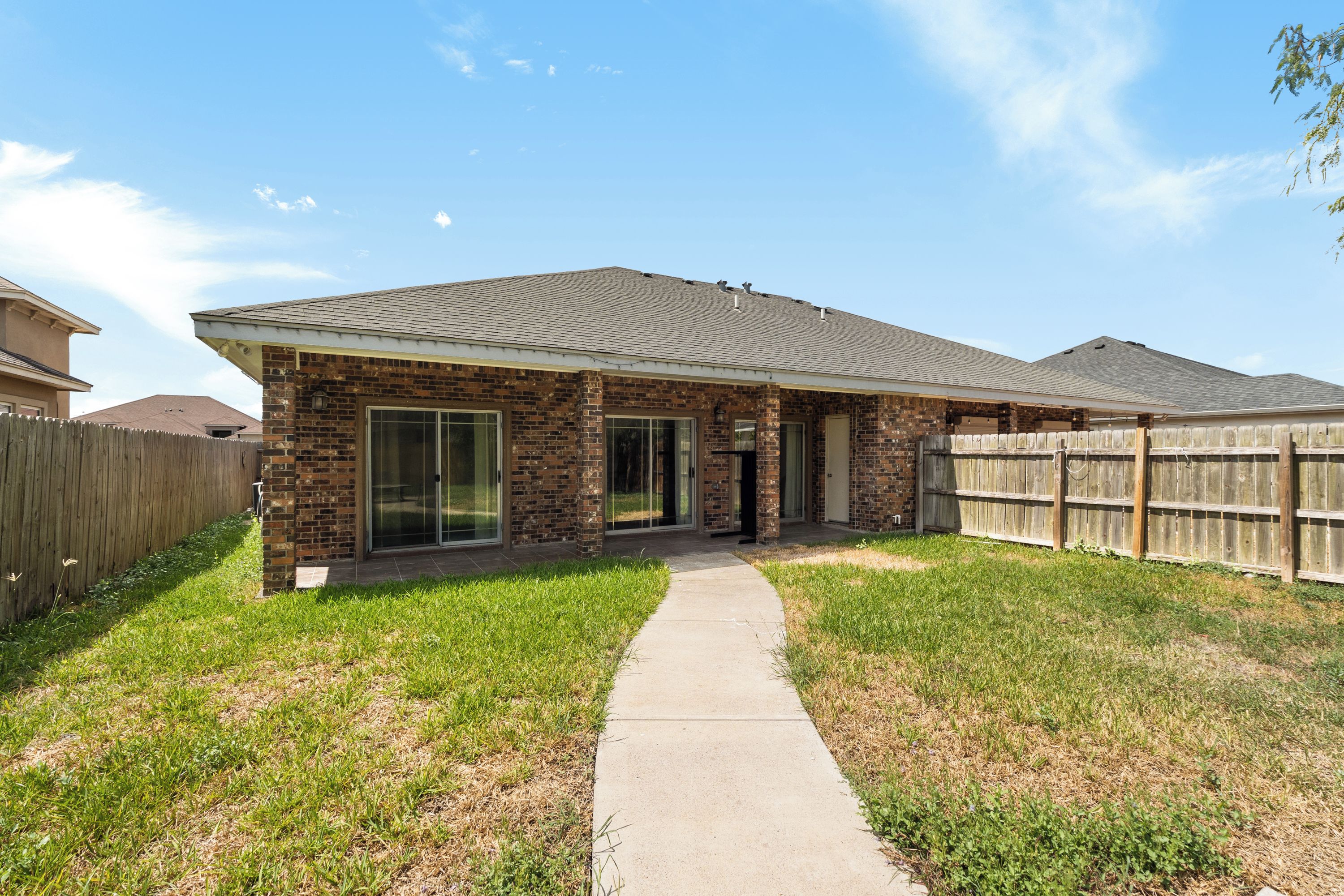 A single-story house with a brick facade, a covered patio, and a fenced backyard.