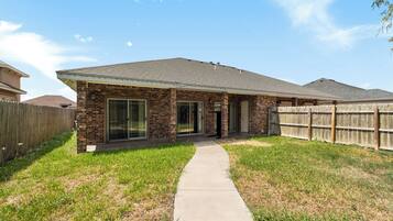 A single-story house with a brick facade, a covered patio, and a fenced backyard.