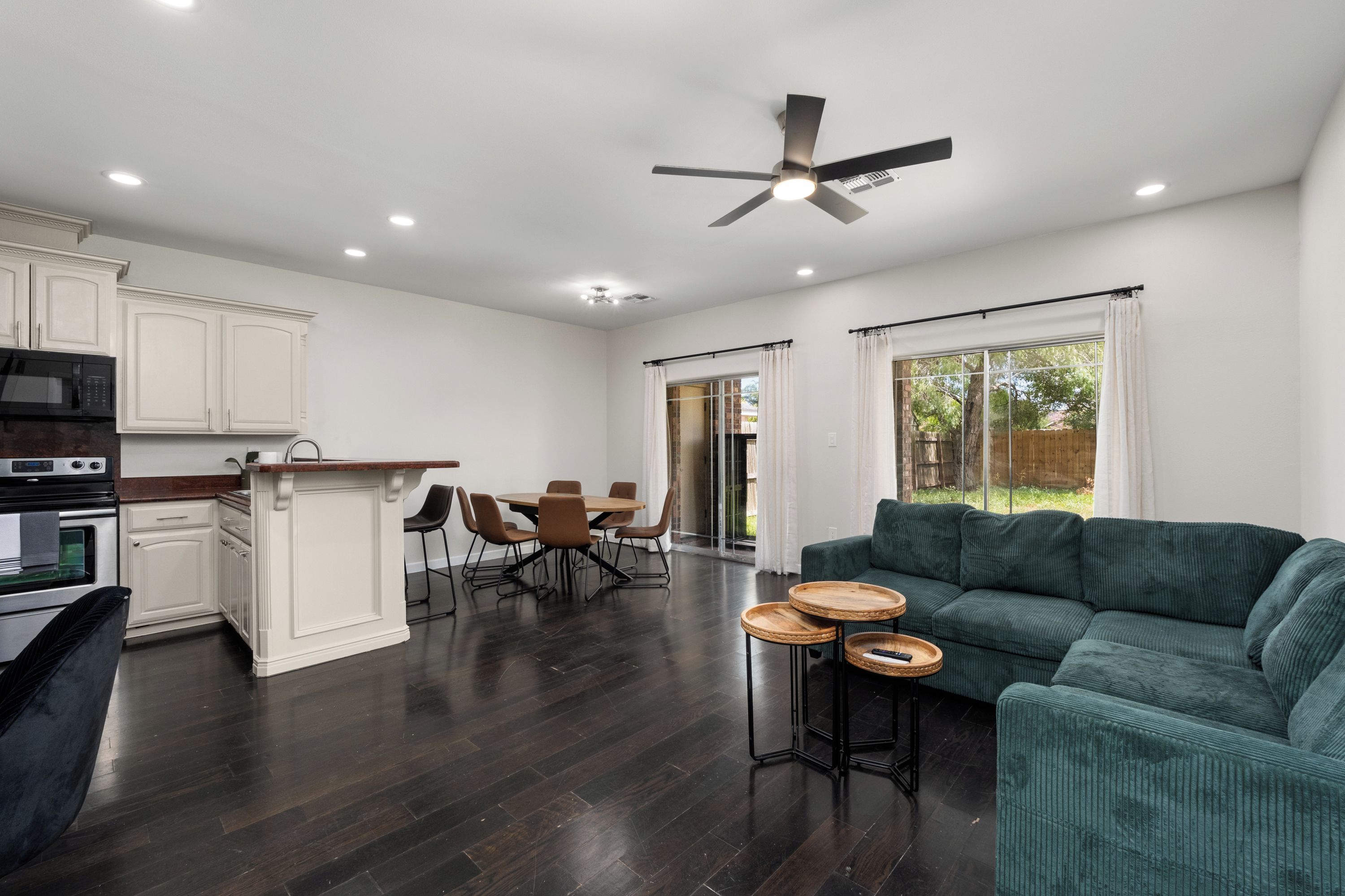 A spacious living area with a dark wood floor, a green sofa, and a dining table with chairs.