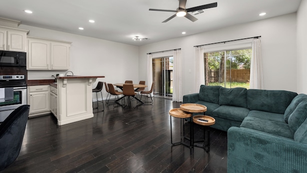 A spacious living area with a dark wood floor, a green sofa, and a dining table with chairs. - The A Lux Backyard House | 3BR w Private Backyard (Brownsville)