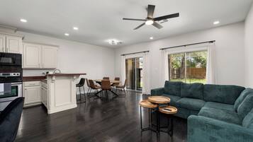 A spacious living area with a dark wood floor, a green sofa, and a dining table with chairs.