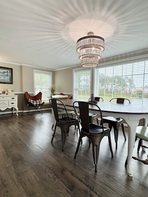 A dining area with a chandelier, wooden flooring, and a view through large windows.