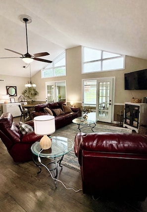A spacious living room with a ceiling fan, a large window, and a flat-screen TV mounted on the wall. - The Pungo Perch: Waterfront Retreat with Boat Lift, Fishing & Pets Welcome (Belhaven)