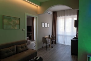 A living room with a sofa, a dining table with chairs, a TV, and a window with curtains. - VELARIS LUXURY SUITE & SPA - Self-Check-In (Bologna)