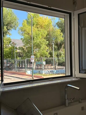 A window with a view of a park, including trees, a fence, and a playground. - Parkside Residence (Vironas)