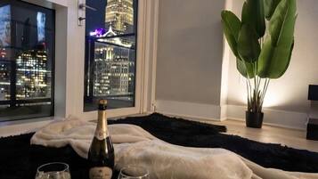 A room with a view of a city skyline, a bottle of champagne, two glasses, and a large plant.