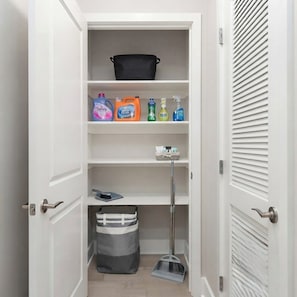 Un placard de rangement propre et bien organisé, avec des étagères contenant des produits de nettoyage, une serpillière et un sac à ordures.