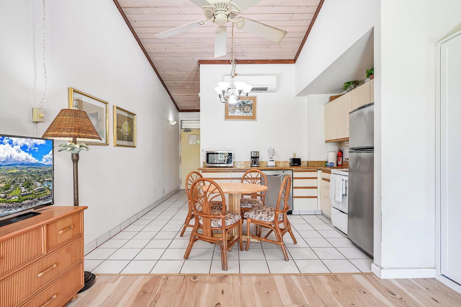 A modern kitchen with white cabinets, a stainless steel refrigerator, and a dining area with wicker chairs.