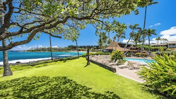 A resort with a swimming pool, lush green lawn, and a view of the ocean.