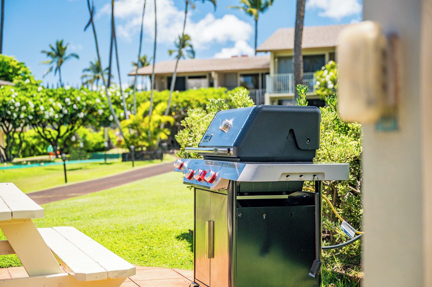 A barbecue grill with a control panel, a picnic table, and a view of a pool and buildings in the background.