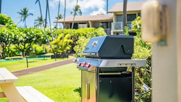 A barbecue grill with a control panel, a picnic table, and a view of a pool and buildings in the background.