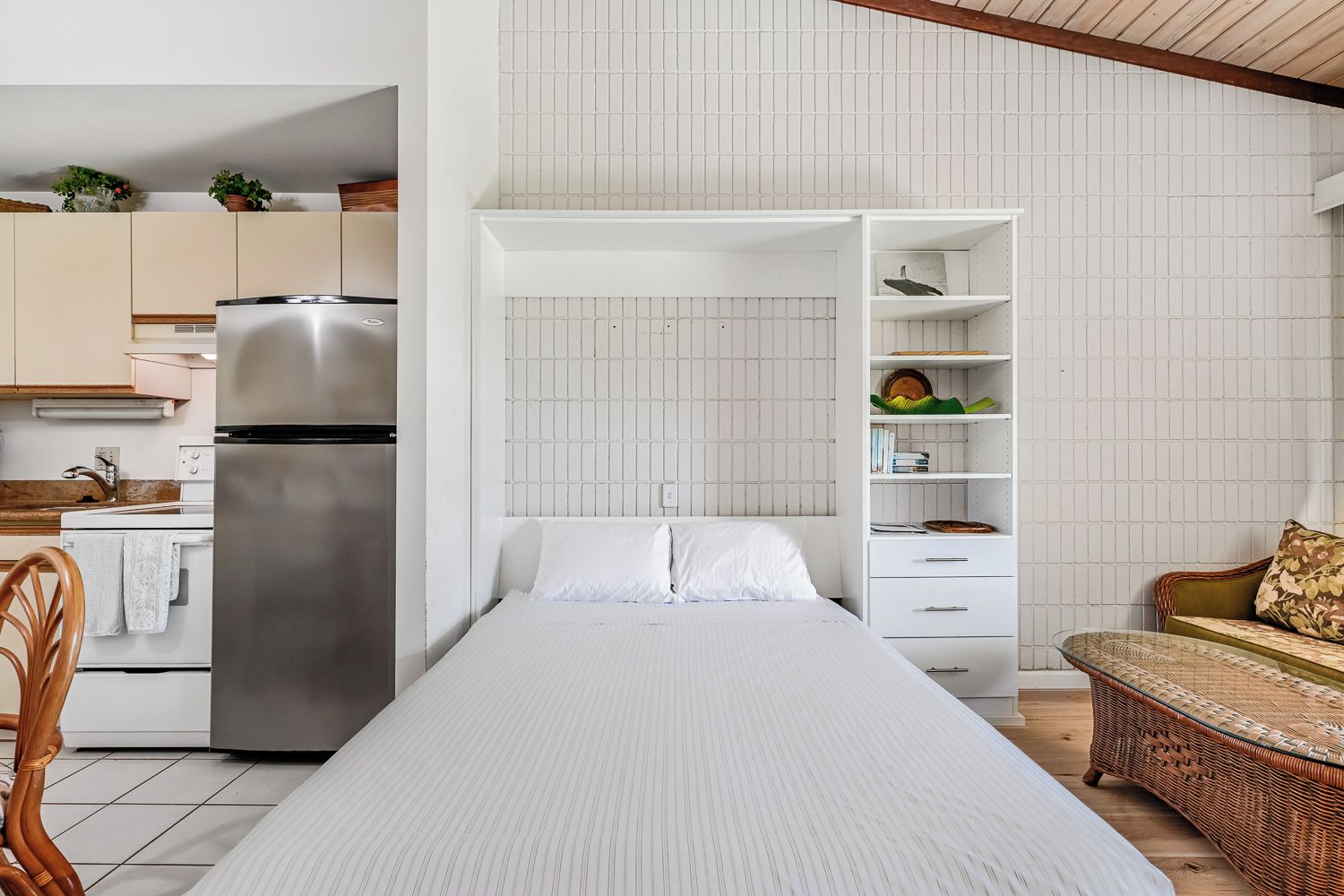 A compact room with a bed, kitchenette, and a seating area with a sofa and a wicker table.