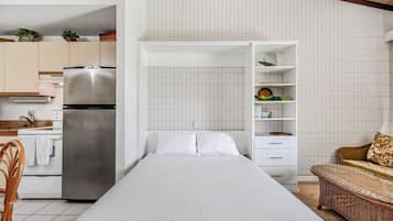 A compact room with a bed, kitchenette, and a seating area with a sofa and a wicker table.