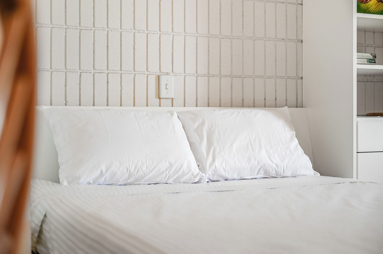 Un lit avec une literie et des oreillers blancs, une tête de lit blanche et un mur blanc orné d’un motif quadrillé.