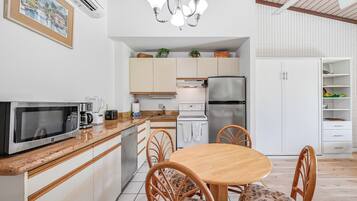 A compact kitchen with a microwave, toaster, and refrigerator. There is a dining table with chairs and a chandelier above.