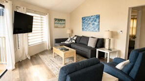 Ein Wohnzimmer mit einer Couch, einem Couchtisch, einem Fernseher und einem Gemälde an der Wand.