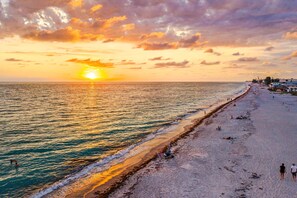 Ein Strand mit Sonnenuntergang, ruhiger See und Menschen, die spazieren gehen.
