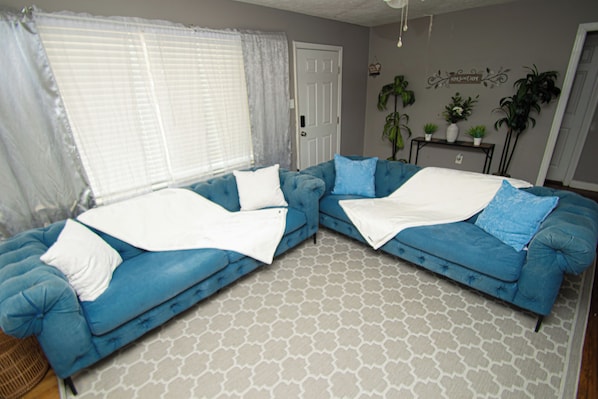 A living room with a blue sofa set, a patterned rug, and a door.