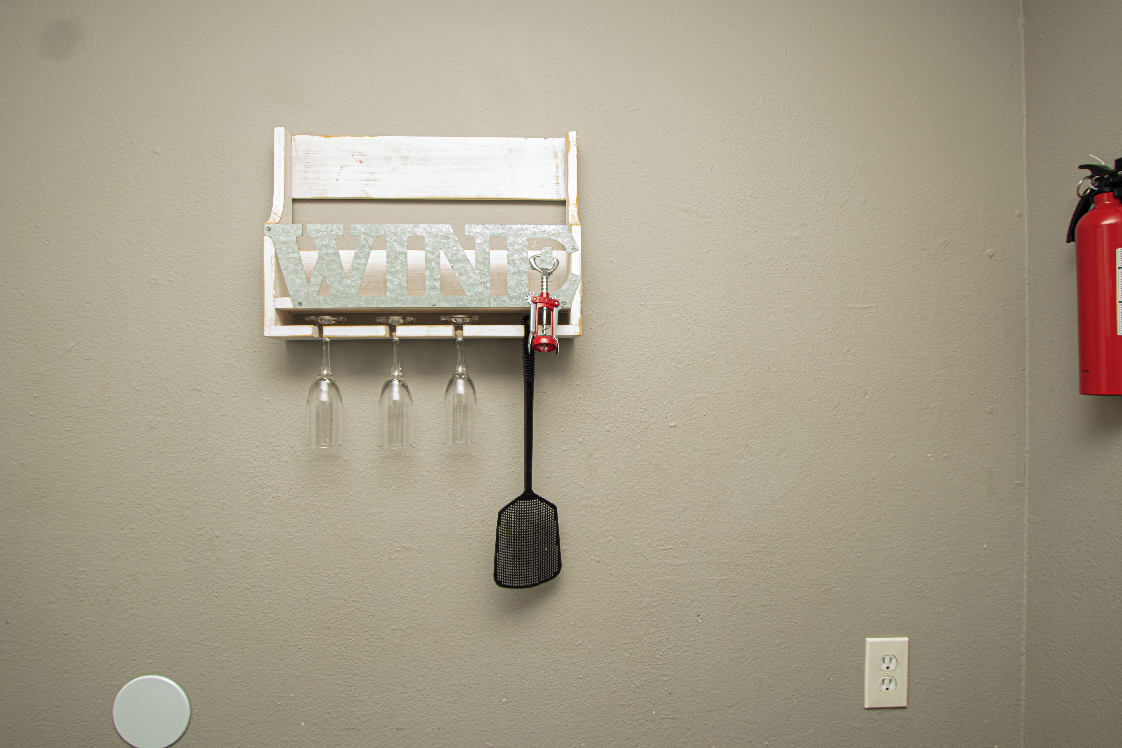 A wall-mounted wine rack with three glasses and a corkscrew.