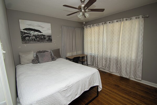 A bedroom with a bed, a desk, a ceiling fan, and a window with curtains.