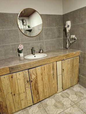 Un bagno con un mobile bagno in legno, uno specchio rotondo, un lavandino bianco e un asciugacapelli a parete.