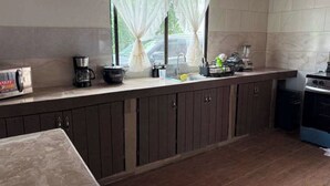Eine Küche mit Arbeitsplatte, Schränken, einem Herd, einer Kaffeemaschine und einem Fenster mit Vorhängen.