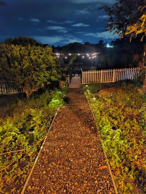 Un sentiero conduce a un edificio, con un recinto in legno da un lato e un giardino dall'altro.