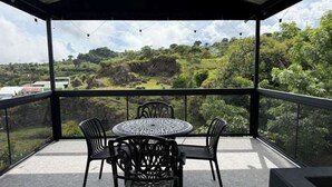Ein überdachter Außenbereich mit Tisch und Stühlen, der einen üppigen Ausblick bietet.