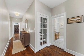 A hallway with a wooden floor, a rug, a cabinet with a mirror, and a door leading to a room. - The Arch House – 4BR – Midtown – Game Loft + Fire Pit (Columbus)