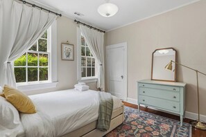 A bedroom with a bed, a dresser, a mirror, and a window with curtains. - The Arch House – 4BR – Midtown – Game Loft + Fire Pit (Columbus)