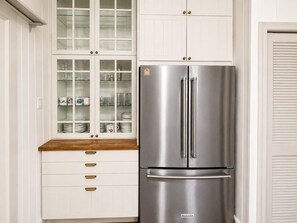 A kitchen with a stainless steel refrigerator, white cabinetry, and a wooden countertop. - The Arch House – 4BR – Midtown – Game Loft + Fire Pit (Columbus)