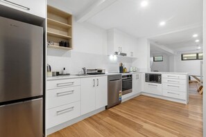 A modern kitchen with white cabinetry, stainless steel appliances, and a wooden floor. - Banksia on the Beach (Gold Coast)