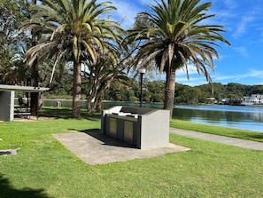 A park with a concrete seating area, palm trees, and a lake. - Banksia on the Beach (Gold Coast)