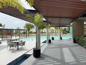 A poolside area with a covered seating area, a pool, and surrounding greenery. - Resort Style - Pools, Artificial BEACH, Balcony, Fishing Lake, Gulf Club, Gym (Punta Cana)