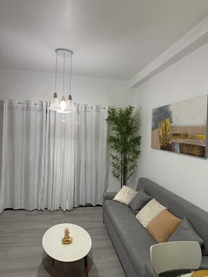 Un salon moderne avec un canapé gris, une table basse ronde blanche et un luminaire suspendu.
