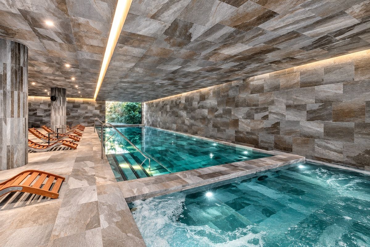 A swimming pool with a stone wall and lounge chairs.