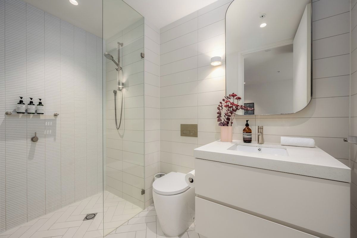 A modern bathroom with a glass-enclosed shower, a white toilet, and a vanity with a mirror.