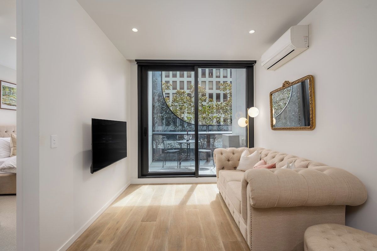 A modern living room with a large window, a flat-screen TV, a sofa, and a mirror.