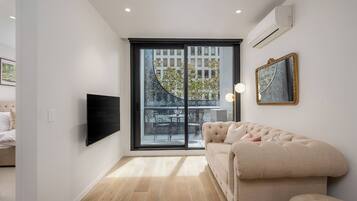 A modern living room with a large window, a flat-screen TV, a sofa, and a mirror.