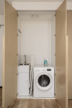 Ein kleiner Waschraum mit einer Waschmaschine mit Frontlader, einem Wäscheständer und einer kleinen Arbeitsfläche mit Waschbecken.